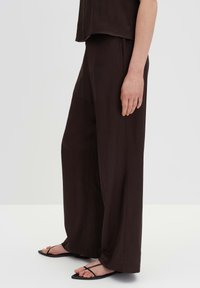 Brown wide-leg trousers with a smooth texture, featuring a relaxed fit and a flowing design. Paired with black strappy sandals.
