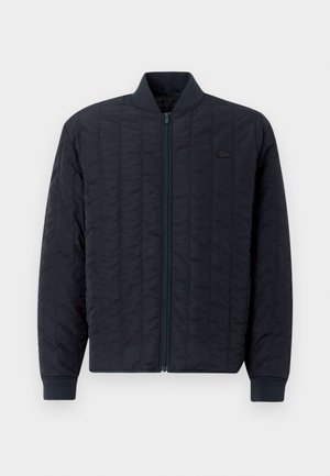 Marineblau gesteppte Jacke mit Reißverschluss vorne, geripptem Kragen und Bündchen, die ein dezentes Logo auf der linken Brust zeigt. Glatte Textur.