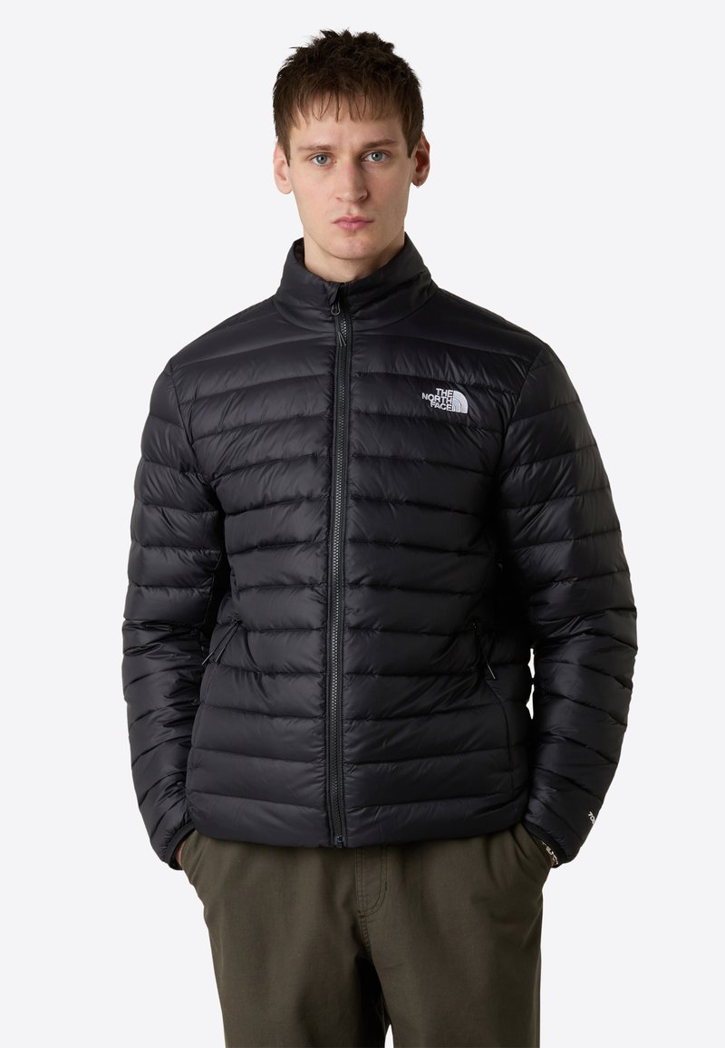 Giacca a vento nera con motivo trapuntato orizzontale, colletto alto, zip completa e logo sul lato sinistro del petto. Tessuto leggero e isolante.