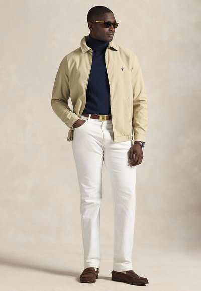 Casaco leve bege, gola alta azul-marinho, calças brancas, sapatos de camurça castanhos; óculos de sol, cintura elástica e detalhe de logótipo no casaco.