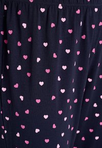 Marineblauwe stof met een verspreid patroon van kleine roze en lichtroze harten. Elastische tailleband voor comfort en een relaxte pasvorm.