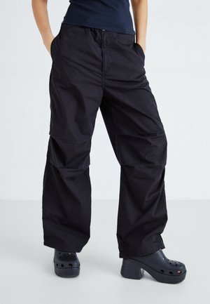 Pantalons cargo noirs avec une coupe décontractée, dotés de poches latérales et d'une texture tissée lisse. Associés à des sabots noirs à plateforme.