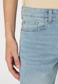 Light blue denim jeans with a fitted design, featuring a front pocket, button details, and a slightly faded texture.