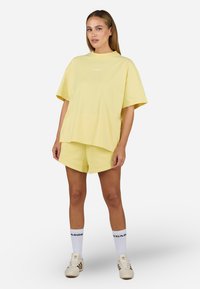 Gul oversized t-skjorte i bomull med korte ermer og rund hals, sammen med matchende gule shorts, med minimal merkevare.