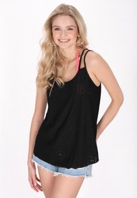 Top senza maniche nero con una trama decorativa e spalline rosa, abbinato a pantaloni shorts di denim chiaro con orli sfrangiati.
