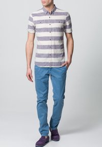 Kortärmad randig skjorta i krämfärgad och lila, med knapp-down krage, och två bröstfickor; matchad med blå byxor och lila skor.