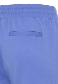 Vue arrière d'un pantalon bleu clair à taille élastique montrant une poche passepoilée unique sans fermeture visible.