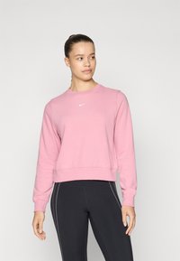 Sweatshirt Nike rose avec un col rond, des poignets côtelés et un logo discret. Associé à des leggings noirs avec des rayures blanches sur les côtés.