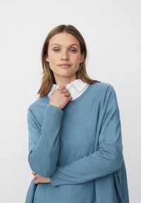 Jasnoniebieski sweter z długim rękawem o prążkowanej strukturze, z szerokim dekoltem i luźnym krojem, noszony na białej koszuli z kołnierzykiem.