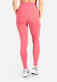 High-waisted legging in felroze, gemaakt van rekbaar materiaal. Heeft een gladde textuur en een aansluitend ontwerp, gecombineerd met witte sneakers.
