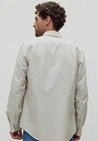 Ljusgrå button-up skjorta med krage, långa ärmar och synlig sömdetalj. Slät textur med en något avslappnad passform.