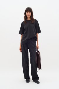 Maglietta nera oversize con maniche corte e scollatura rotonda, abbinata a jeans scuri a gamba dritta e una borsa a tracolla marrone.
