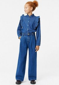 Outfit in denim composto da una camicia a bottoni con volant e colletto, abbinata a jeans a gamba larga e alta vita, entrambi in una tonalità di blu medio.