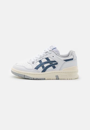 Witte sportieve schoen van synthetisch materiaal, met marineblauwe accenten, geperforeerde neus en een getextureerde rubberen zool voor grip.