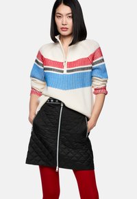 Knit sweater with a quarter zip, featuring red, blue, and black stripes; paired with a black quilted skirt with a front zipper and red tights.