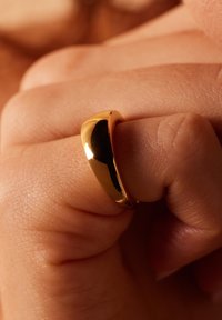Gouden ring met een glad, afgerond ontwerp op een hand, die de gepolijste textuur en glanzende oppervlakte toont.