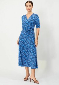 Sininen kukkakuosisekoitteinen mekko, jossa on lyhyet hihat, V-pääntie, istuva vyötärö ja hulmuava midi-pituinen hame, yhdistettynä ruskeisiin korkokenkiin.