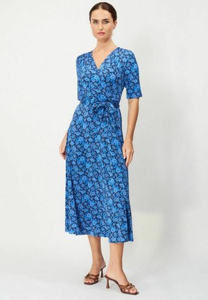 Blå blommig wrapklänning med korta ärmar, v-ringning, figursydd midja och ett svängande midi-långt kjol, kombinerad med bruna klacksandaler.