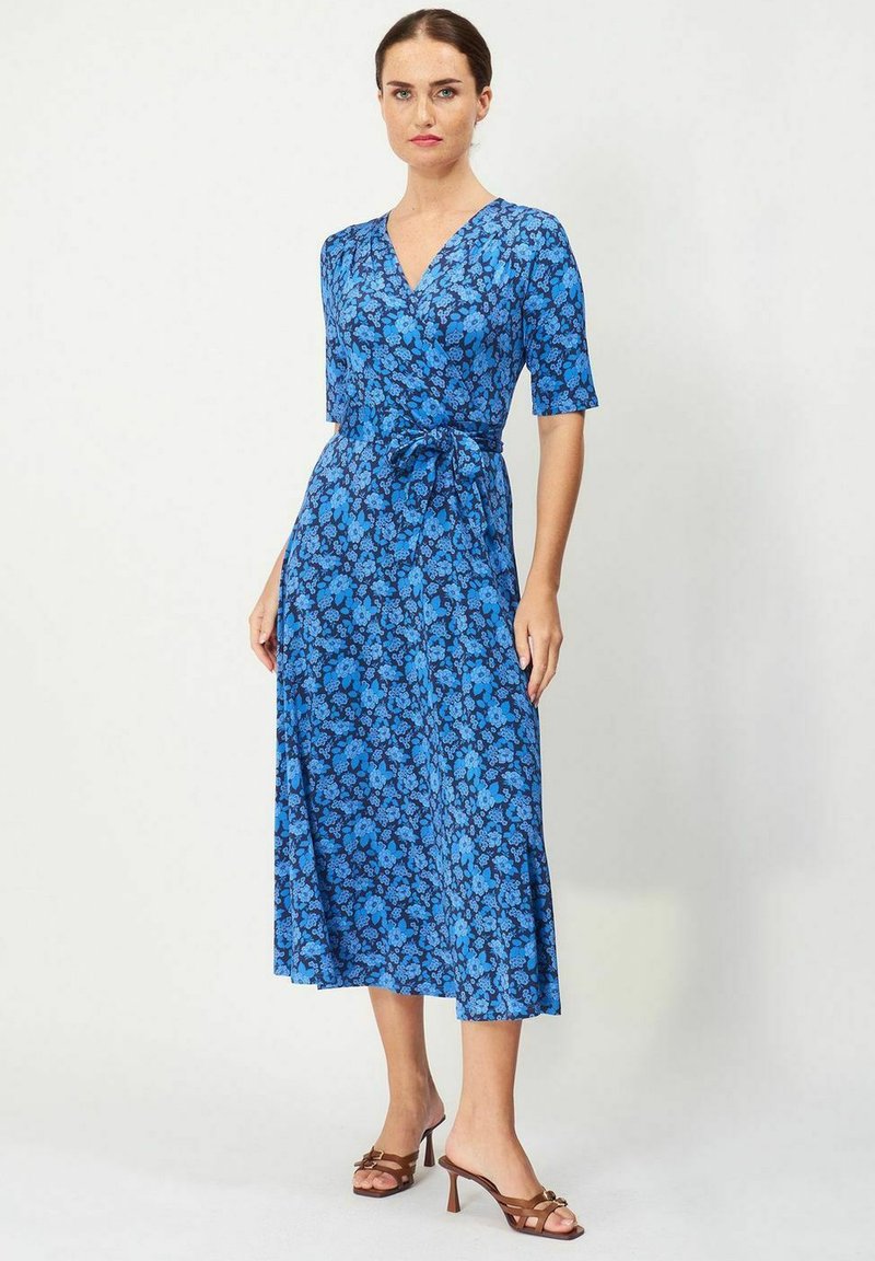 Sininen kukkakuosisekoitteinen mekko, jossa on lyhyet hihat, V-pääntie, istuva vyötärö ja hulmuava midi-pituinen hame, yhdistettynä ruskeisiin korkokenkiin.