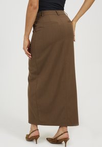 Bruine, hoge maxi-rok met een gladde textuur, twee achterzakken en subtiele naden, gecombineerd met lederen print hakken.