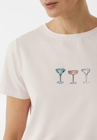 Light pink t-shirt featuring a printed design of three cocktail glasses in blue, orange, and white, with minimalistic outlines and details.