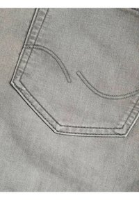 Szary dżinsowy materiał z sześciokątną kieszenią ozdobioną subtelnymi przeszyciami, w tym zaokrąglonymi akcentami i teksturowaną powierzchnią.