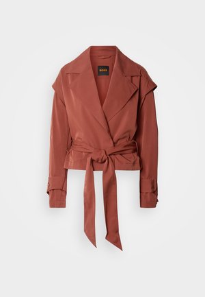 Roostevärvi vööga jakk laiade kraeäärte, pikkade varrukatega, varrukatel mansettrihmad ning lõdva istuvusega, ripub valge tausta ees.