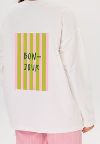 Wit sweatshirt met lange mouwen, voorzien van een groen, roze en gele gestreepte rechthoekige graphic met "BON-JOUR" in zwart gedrukt.
