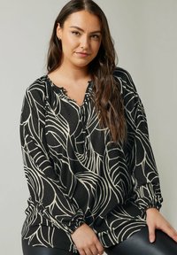 Blusa nera a maniche lunghe con motivi a foglia color crema, dotata di colletto rotondo e dettagli con bottoni, realizzata in un morbido tessuto testurizzato.