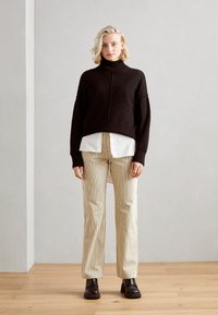 Must mustriga turtleneck-sweater musta, valge särk; beežiriba lai-püksid; jämedad mustad ankle saapad; minimalistlik taust.