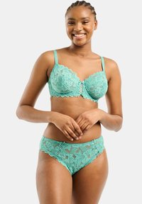 Il reggiseno in pizzo turchese e le mutandine abbinate presentano motivi floreali, bordi scallop e una consistenza morbida, con spalline regolabili e dettagli decorativi.