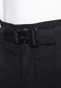 Zwarte broek met een structuurtstof, een stevige zwarte gesp en een strakke trekkoord. Stiksels zijn zichtbaar langs de taille.