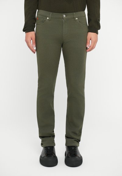 Oliven grønn jeans med slim fit, der har fem lommer, lynlås og hardware i sølvfarve. Parret med sorte sneakers.