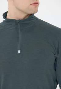 Donkergrijze lange mouw pullover met een ritskraag, gekenmerkt door een gladde textuur en een subtiel gemêleerd patroon. Reflecterend logo detail op de kraag.