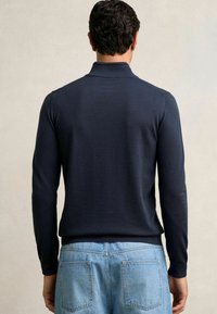 Marineblaue Langarm-Poloshirt mit einer weichen Textur, ausgestattet mit einem kragen und gerippten Bündchen, kombiniert mit hellblauen Jeans.