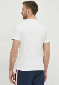 T-shirt bianca a maniche corte realizzata in cotone, con scollo rotondo e sottili accenti rossi sulle maniche, vista da dietro.