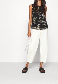 Haut sans manches noir à motifs floraux avec un voile transparent, assorti à un pantalon large blanc et des sandales à glisser noires. Petit sac tissé inclus.