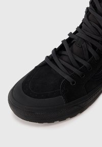 Lähedane vaade mustade kõrgematele sneakeritele, millel on tekstiilse kasutusega kummiseid tallad ning nahast ja kangast pealmine osa.