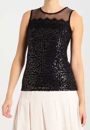 Haut noir sans manches avec un col transparent à pois et un motif pailleté en sequins, associé à une jupe plissée blanche.