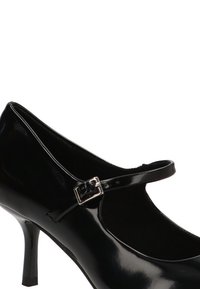 Zapato Mary Jane de charol negro con puntera redondeada, delgada correa en el tobillo y hebilla plateada. Presenta un tacón alto y delgado.