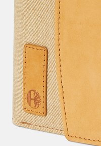 Borsa in tela con dettagli in pelle beige, dotata di un patch con logo e tessuto testurizzato. I colori sono beige e marrone chiaro.