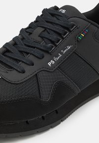 Černé tenisky s kombinací hladké kůže a síťoviny, texturované prvky, ploché černé tkaničky a decentní detail loga.