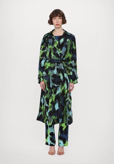 Trench coat lungo e lavorato nei colori nero, verde e blu, stretto in vita da una cintura. Abbinato a pantaloni a motivi blu e verde coordinati.