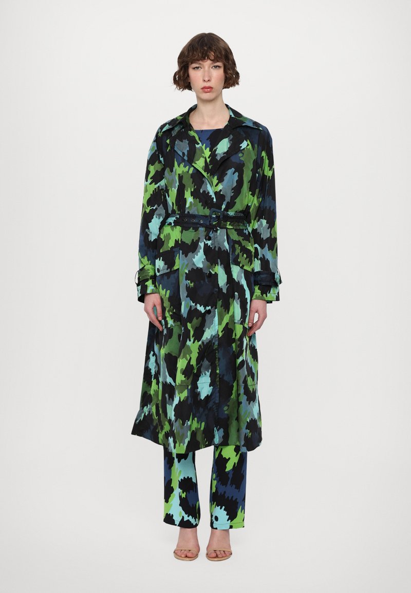 Long, patterned trench coat in black, green, and blue, cinched at the waist with a belt. Paired with matching blue and green patterned pants.