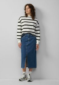 Witte longsleeve top met zwarte strepen, gecombineerd met een blauwe denim midi rok met een voorknos, gedragen met grijze sportschoenen.
