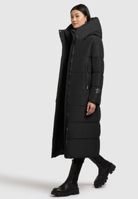 Sort polstret lang frakke med høj krave, lynlås lukning og sidelommer. Har et strømlinet design og tekstureret stof med en blank finish.
