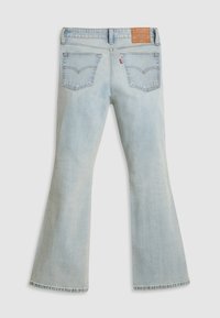 Vaqueros acampanados de color azul claro con una textura de denim desgastado, costuras visibles, dos bolsillos traseros y una etiqueta de cuero en la cintura.