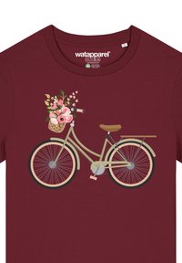 Graphique de bicyclette sur un t-shirt bordeaux ; le vélo est vert clair avec un siège marron et un panier à fleurs, orné de motifs floraux roses et blancs.