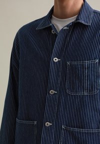 Navy blue striped work shirt, made of textured fabric, featuring a button-down front, two front pockets, and contrasting white stitching.