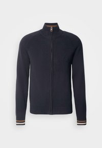 Pull en maille bleu marine à fermeture éclair intégrale, col montant et poignets côtelés avec des rayures marron et blanches.